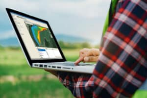 Farmer in a field holding a laptop whilst looking at data in Trimble Ag Software