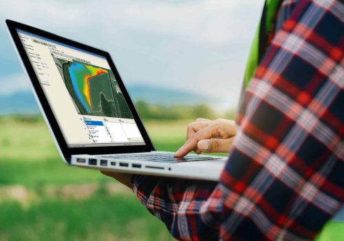 Farmer in a field holding a laptop whilst looking at data in Trimble Ag Software